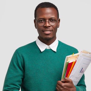 Indoor shot of pleased dark skinned successful man dressed elegnatly, carries documentation, glad to recieve praise from boss for well prepared financial report, stands against white background